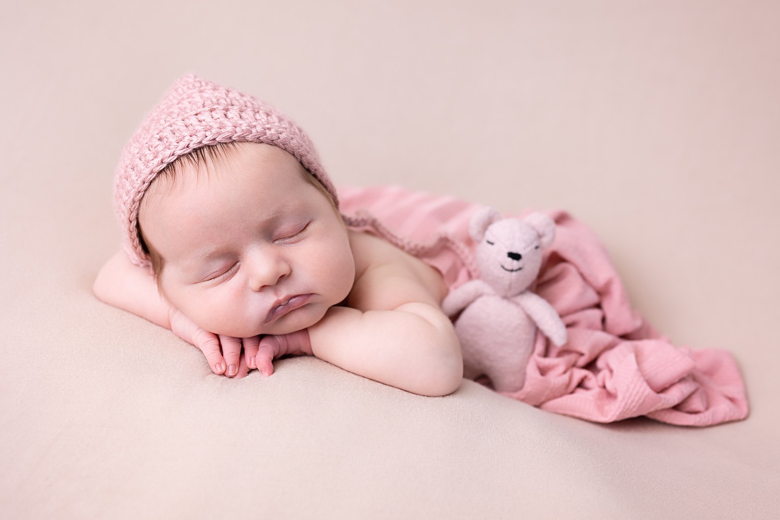 newborn baby in a relaxed chin on hats pose with woolen hat with teddy in warm cosy studio in royston hertfordshire near cambridge